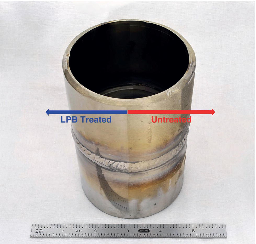 A metal cylindrical object showing two sections. L P B treated on the left and untreated on the right, with a horizontal double-headed arrow pointing between them. A prominent weld is visible around the middle of the cylinder. A ruler is placed at the bottom for scale.