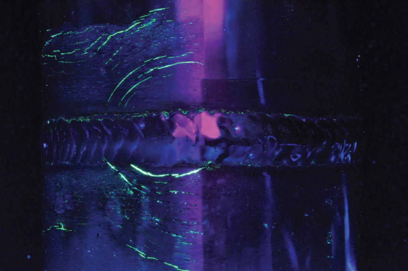 A close-up image of a metal surface featuring a weld seam running horizontally across the center. The seam has a rough texture with visible welding patterns.
