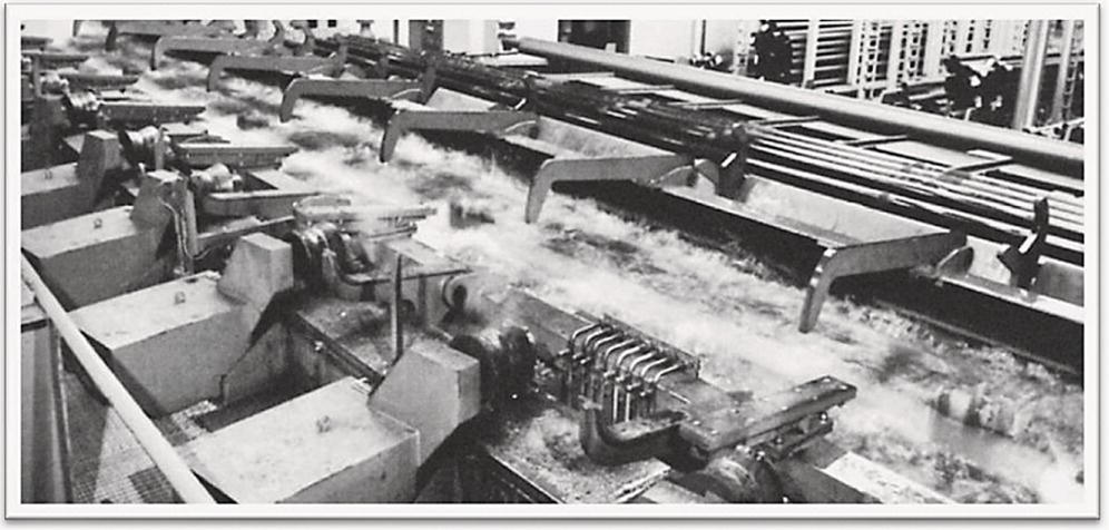 Image of an industrial milling machine processing fibers in a factory setting. The machine features multiple rows of fast-spinning brushes or blades, guiding fibers along the conveyor.
