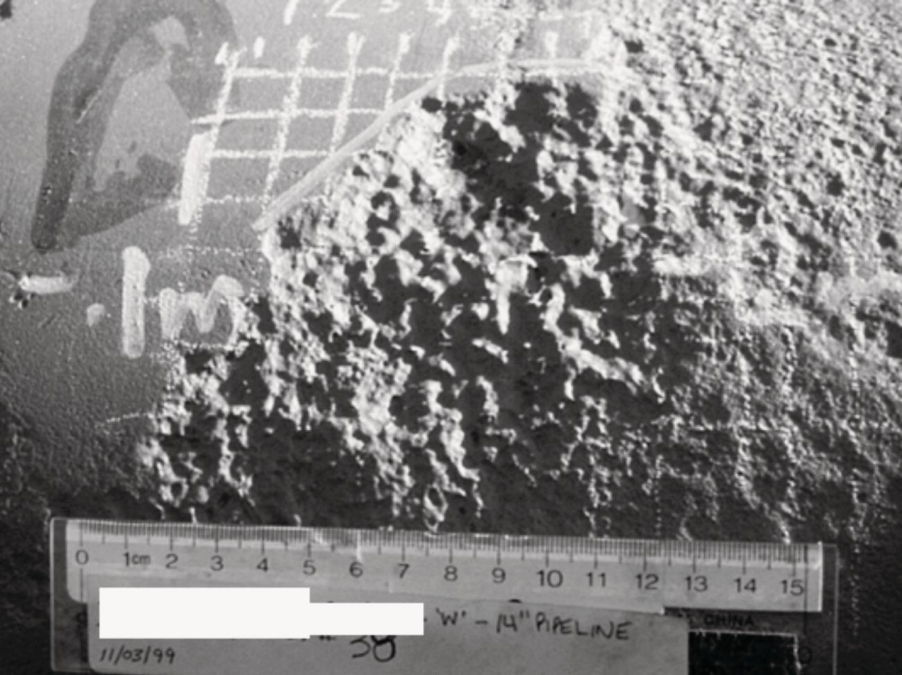 A textured surface appears fragmented, displaying a rough, uneven terrain that resembles a geological feature. The lower part includes a ruler for scale, measuring in centimetres, with markings clearly visible. Above the ruler, handwritten annotations include notations such as W 14 Pipeline, and additional numerical data. A grid pattern with faint lines overlays the scene, providing a reference framework. The context suggests a scientific or engineering evaluation, potentially related to geological studies or pipeline inspections.