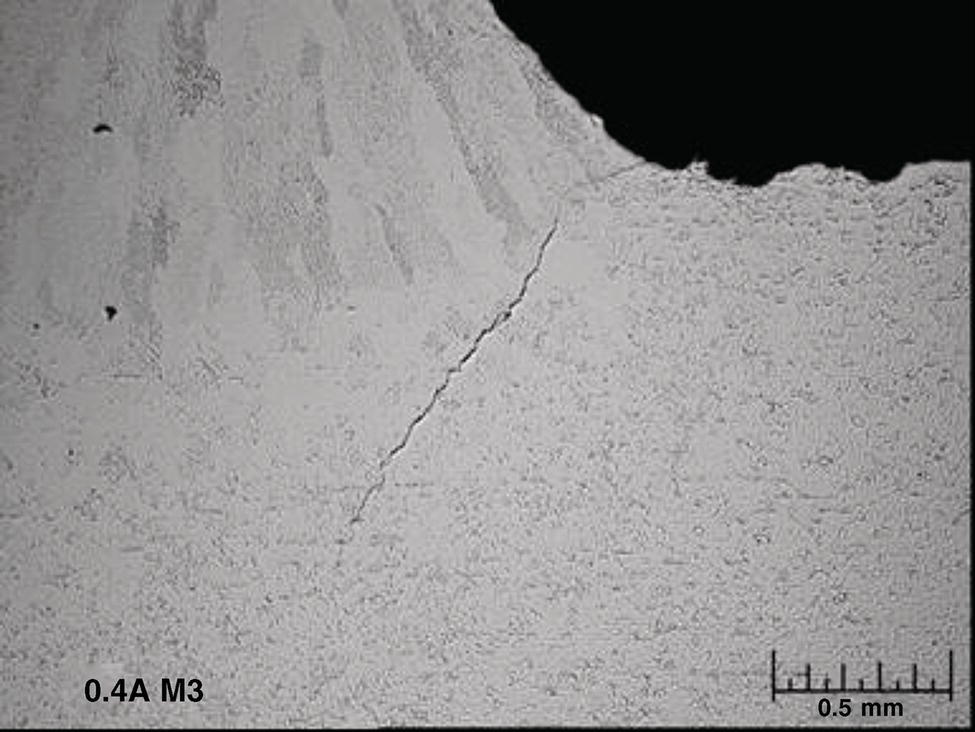 A microscopic image presents a magnified view of a material sample with a visible crack or fracture line running through it. The surface has a textured, grainy appearance typical of metallurgical or geological samples. In the upper right corner, there’s a darker region that may indicate a void or different material phase. The bottom left corner contains the text 0.4 Angstrom M 3, likely indicating the sample identification or magnification parameters. A scale bar in the bottom right reads 0.5 m m, providing measurement reference for the features visible in the image.