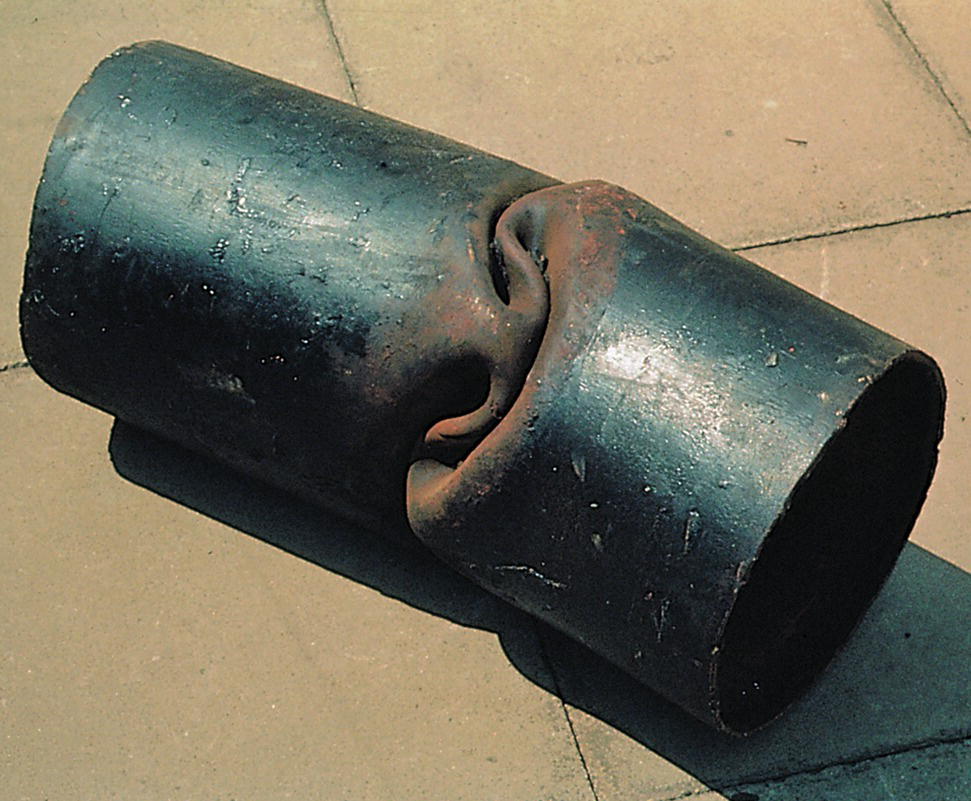 A close-up captures the intricate details of a silver axle. The texture is smooth with subtle reflections. Positioned on the ground, the axle stands resiliently in an outdoor setting. Surrounding elements include a cylindrical shape resembling a pipe that complements the overall composition.