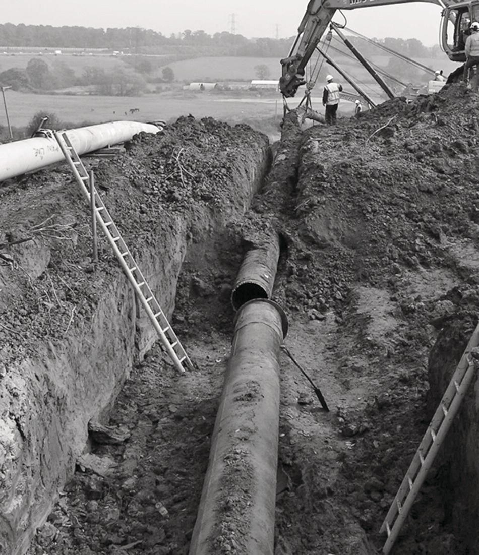 A person holds a pipe against an expansive sky, emphasizing the connection between nature and infrastructure. The outdoor setting is captured in presenting a stark contrast between the dark pipe and the lighter elements of the scene. Pipeline transport is implied through the presence of the pipe resting on the ground, tying together themes of human engineering and natural landscapes.