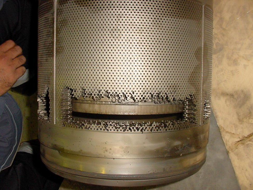 A closer view of a cylindrical metallic filter with visible perforations and corrosion on its edges. A hand is seen nearby, suggesting ongoing maintenance or inspection.