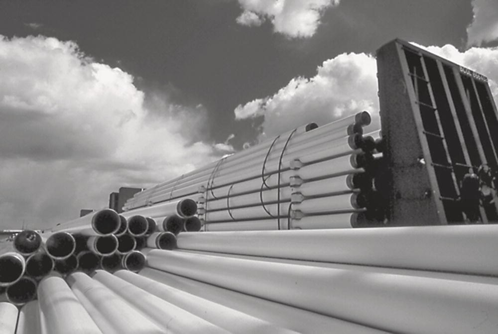 A photograph shows stacks of white pipes arranged on a construction site against a cloudy sky. The image highlights the cylindrical ends of the pipes in the foreground.