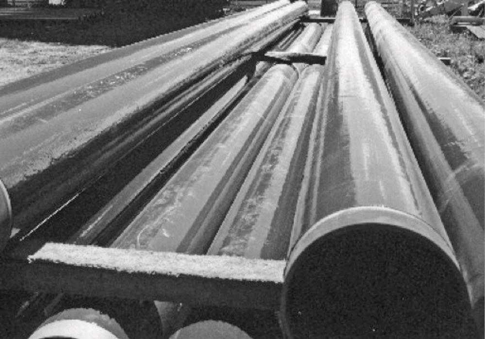 A closer view of several large pipes stacked on a wooden support at a construction site. The image is in black and white, emphasizing the smooth surfaces and cylindrical ends of the pipes.