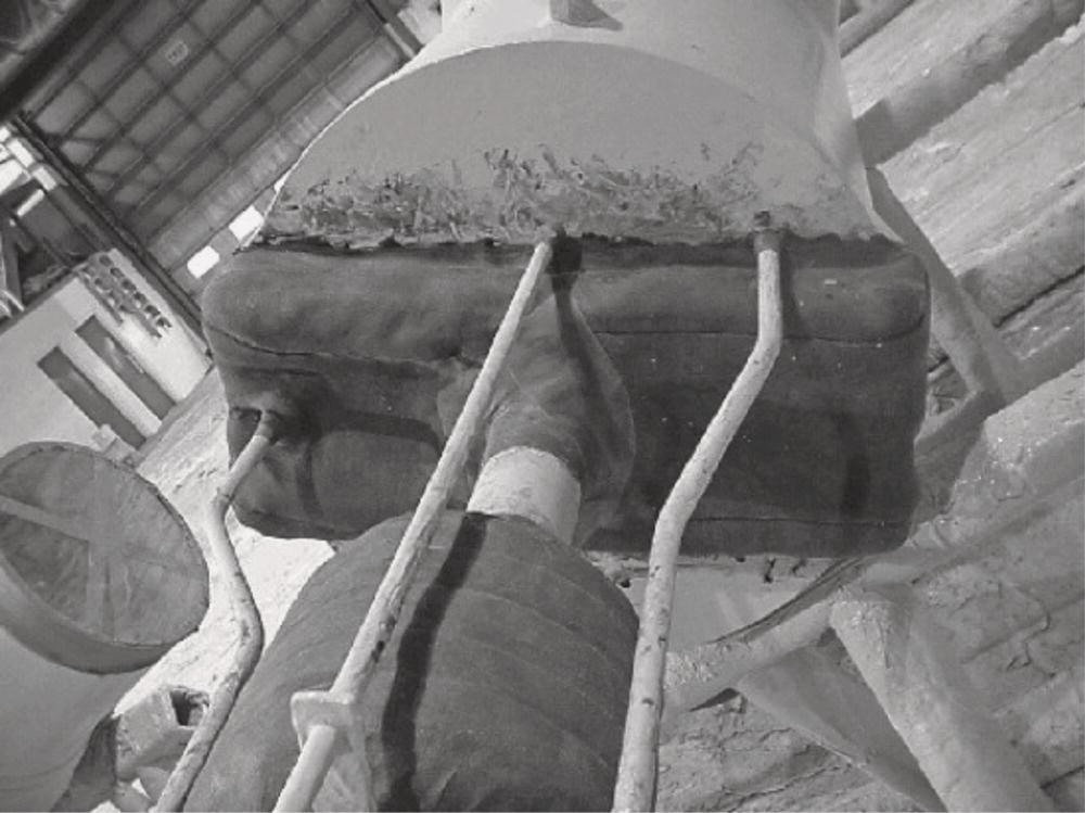 A closer view of a large pipe with protective padding and multiple connected hoses. The image is in black and white, showcasing the textured surface of the padding and the pipe’s fittings.