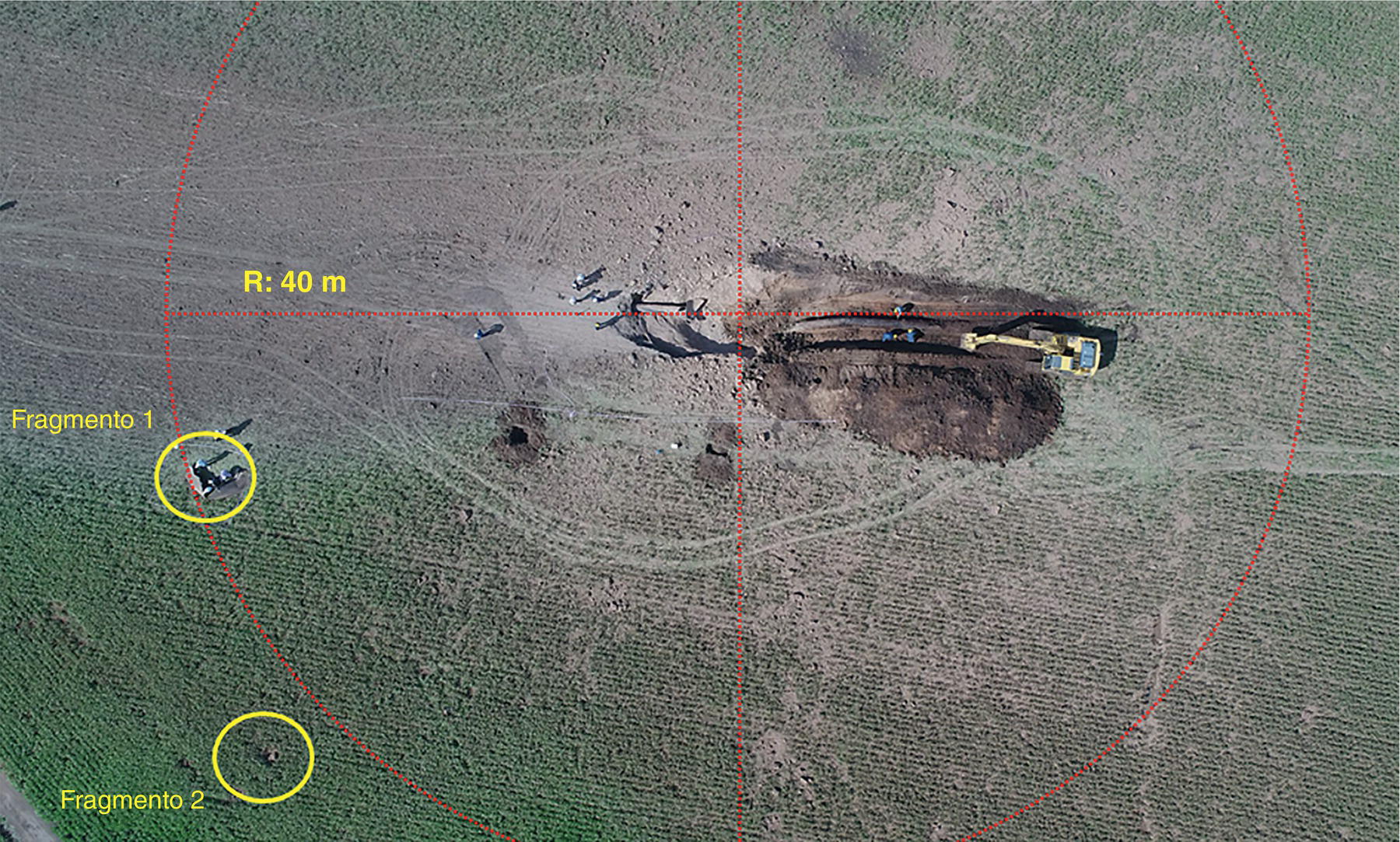 An aerial view of an excavation site with two labeled fragments on a flat surface. A piece of heavy machinery is visible near a large circular area in the center, surrounded by disturbed ground.