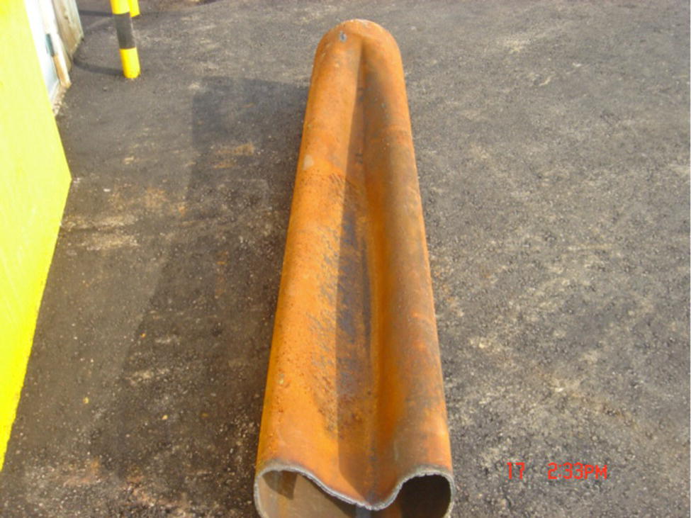 A long, curved piece of pipe lying on a flat surface. The pipe is weathered, with visible wear and a hollow interior.