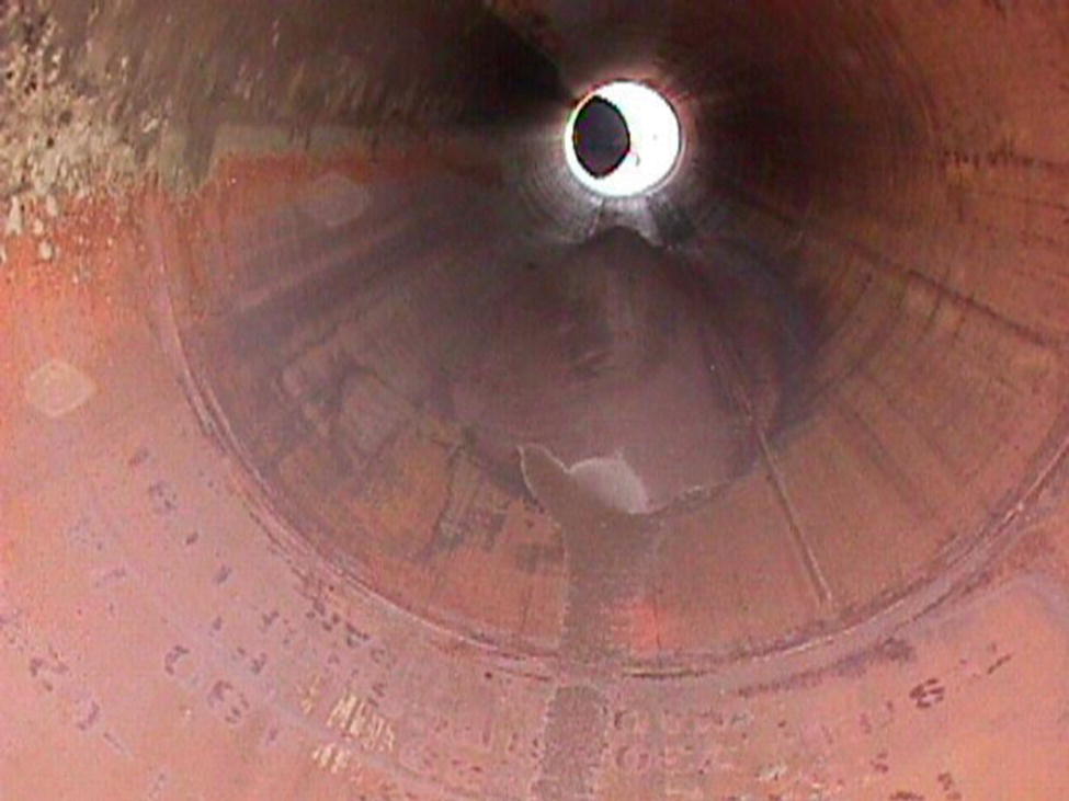 A dark, cylindrical view looking down the interior of a pipe. The surface shows signs of wear, with a faint light visible at the far end.