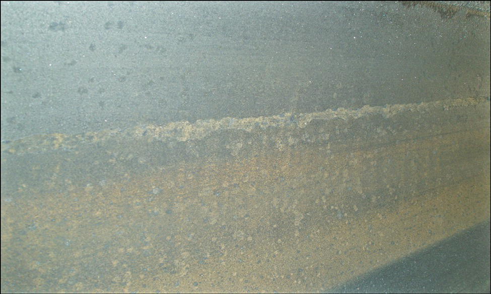 A closer view of a metallic surface, showing a pattern of water droplets and faint scratches. The texture appears smooth but is marked by signs of wear.