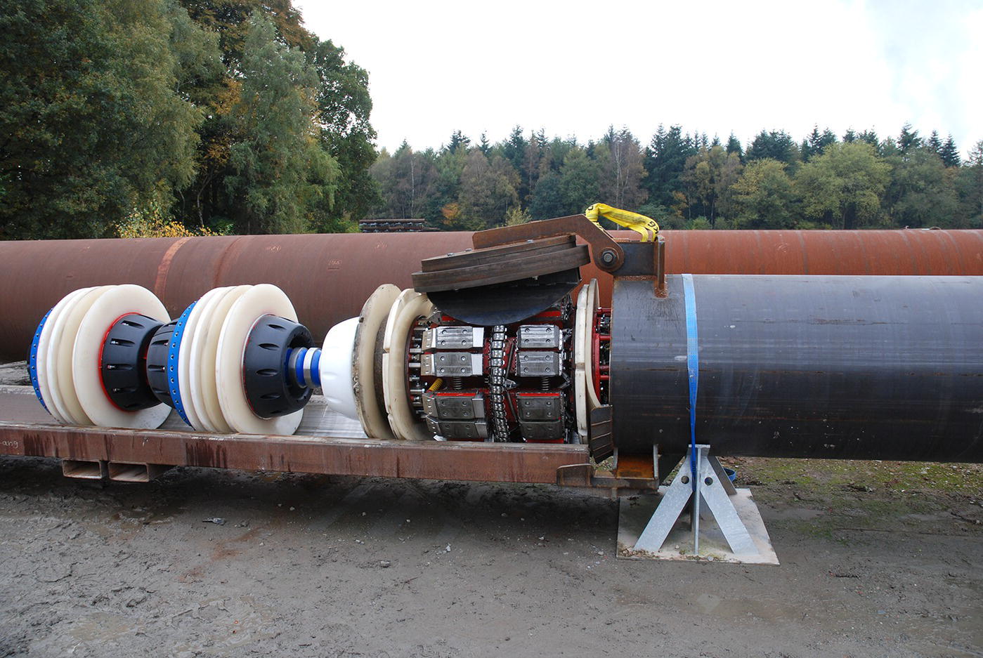A closer view of large industrial pipes with a mechanical device attached. The scene is set in a natural environment with trees in the background.
